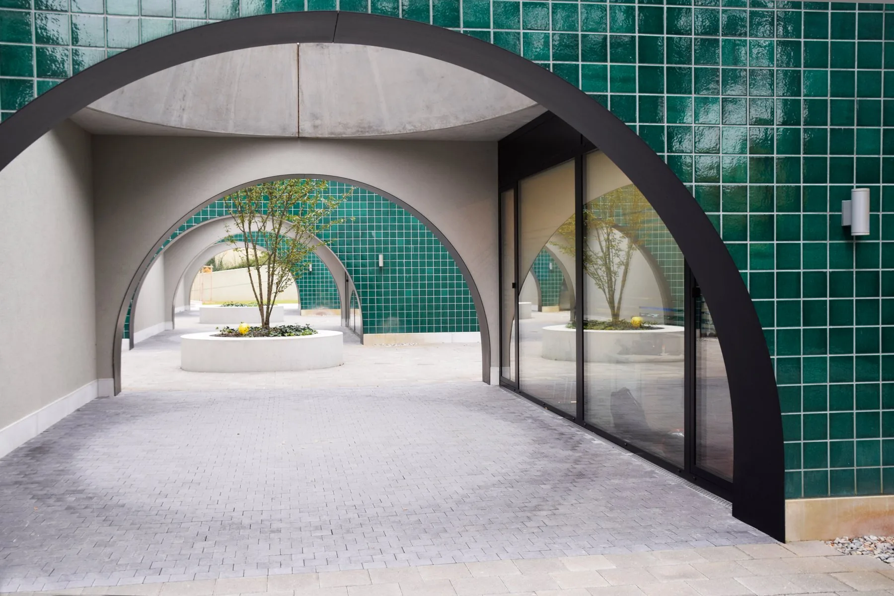 Entrée vitrée encadrée d’arches noires, avec des murs carrelés verts.